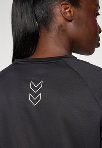 Zwart sportshirt met een geribbelde textuur, ronde halslijn en drie witte chevronontwerpen op de achterkant, nabij de nek.