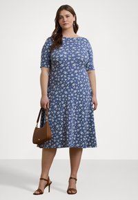 Blå blomstret kjole med korte ermer, A-linje silhuett, laget av bomull. Kombinert med en brun håndveske og brune sandaler med stropper.