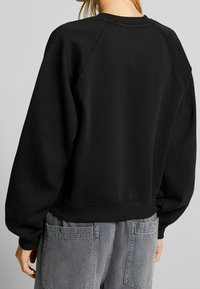 Svart sweatshirt med raglanärmar, texturerad tyg, ribbad krage och fåll. Matchas med grå byxor med hög midja och fickor.