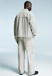 Light gray denim jacket and matching cargo pants, featuring stitched details and pockets, with a relaxed fit and frayed hem accents.