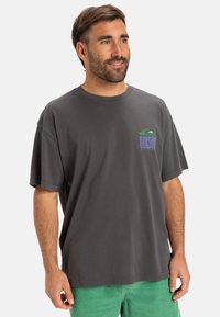 Grijze katoenen t-shirt met korte mouwen en een ronde hals. Bevat een multikleuren logo-opdruk op de linkerborst. Gladde textuur.