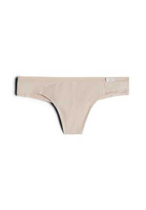 Beżowe bezszwowe stringi z małą białą metką materiałową na pasku, wyświetlone na białym tle.