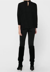 Haut noir avec des manches trois-quarts, détail de dos en trou de serrure, associé à un jean noir ajusté et des bottes hautes en suède noir.