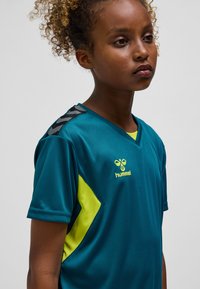 Turkos sporttröja med gula detaljer och V-ringning. Har svarta axelstripes och logotyp, tillverkad av slätt material.