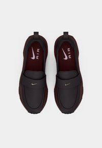 Ett par mörk vinröda Nike Air slip-on sneakers med kardborreband och vita logotypdetaljer, sett uppifrån mot en vit bakgrund.