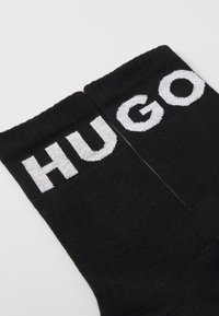 Chaussettes noires avec inscription blanche 'HUGO'. Fabriquées à partir d'un matériau lisse et extensible avec une texture côtelée et un design de longueur classique.