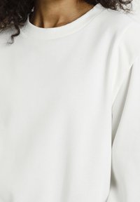 White sweatshirt featuring a crew neckline and ribbed cuffs, made of soft fabric with a smooth texture, showcasing a minimalist design.
