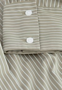 Light brown fabric with thin white stripes, featuring a folded collar and two white buttons, smooth texture with a slight sheen.