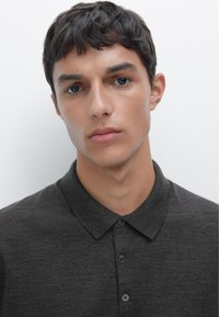 Dunkelgraues Poloshirt mit weicher Textur, ausgestattet mit einem Kragen und einer Knopfleiste mit drei Knöpfen. Minimalistisches Design ohne sichtbare Muster.