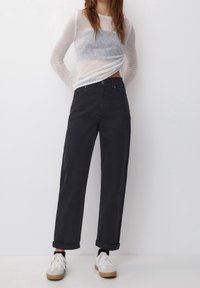 Pantaloni neri a vita alta con un fit rilassato, orli con risvolto e chiusura a bottone, abbinati a una maglia trasparente a maniche lunghe in grigio e bianco.