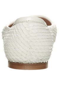 White slip-on shoe with textured reptile-like finish, flat brown sole, rounded back, and smooth edging. Minimalist design emphasizes material.