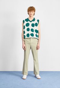 Jersey sin mangas de cuello en V con grandes puntos color teal sobre un fondo crema, combinado con pantalones de cuadros verdes claros y zapatillas blancas.