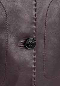 Bordeauxlederstoff mit weicher Textur, kontrastierender Naht und einem schwarzen Knopf mit geprägtem Logodetail.