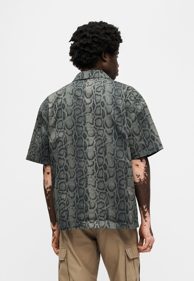 Camicia a maniche corte in tessuto grigio chiaro con motivo stampa serpente scuro; presenta un colletto e un design a vestibilità rilassata.