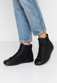 Black high-top sneakers featuring a smooth, textured upper, lace-up front, and a side zipper, with a rubber sole and rounded toe.