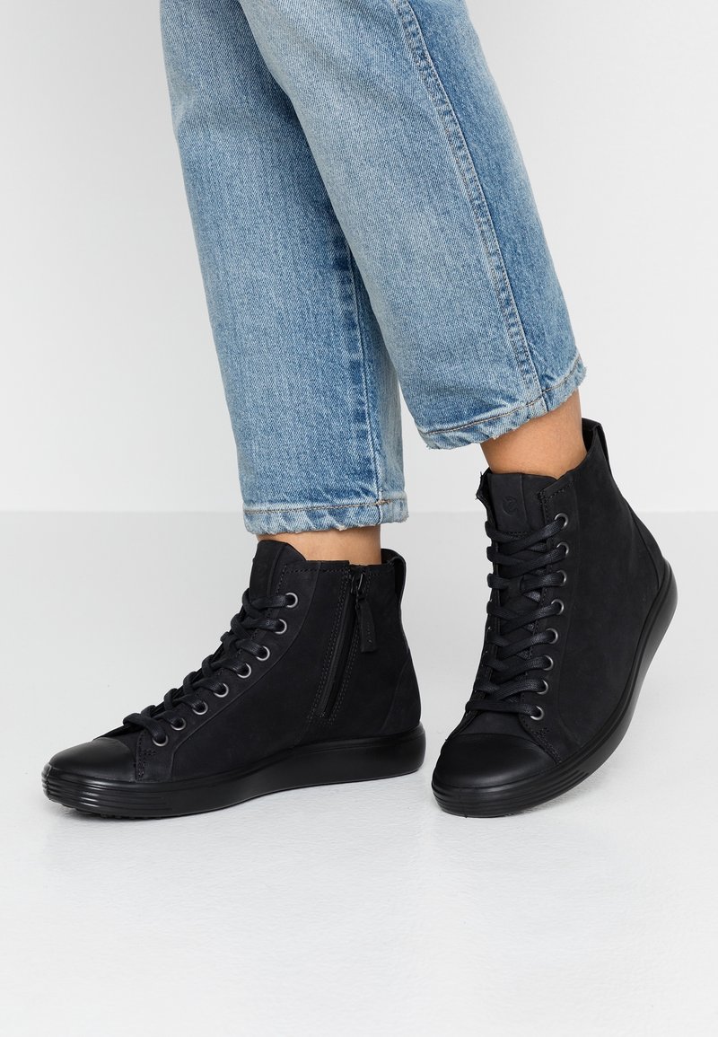 Black high-top sneakers featuring a smooth, textured upper, lace-up front, and a side zipper, with a rubber sole and rounded toe.