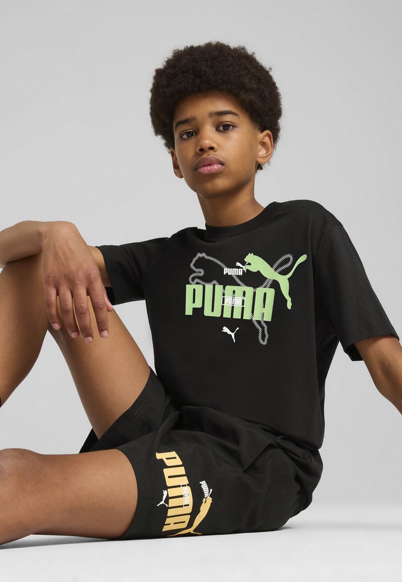 Camiseta negra con logo de Puma en verde y blanco en el frente, combinada con pantalones cortos negros que presentan texto de Puma en amarillo. Material de algodón suave.