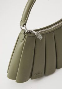 Green pleated handbag made from soft material, featuring a zip closure, curved handle, and a subtle embossed logo. Smooth texture.