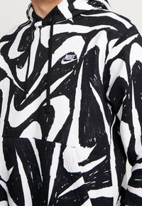 Svart och vit mönstrad hoodie med dragsko i huvan, känguruficka och en liten Nike-logga broderad på bröstet. Blandmaterial i bomull.