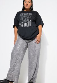 T-shirt grafica nera con il testo "Talking to the Moon", abbinata a pantaloni larghi in paillettes argento, caratterizzati da una texture morbida e lucida.