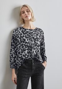 Chemise à boutons en tissu imprimé léopard noir et gris, avec des manches longues et une coupe décontractée. Associée à un jean noir taille haute.