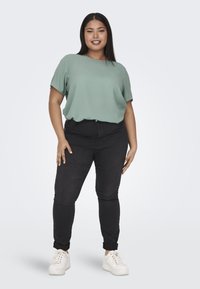 Blusa verde chiaro a maniche corte abbinata a jeans skinny neri, con due tasche anteriori, e sneakers bianche con suole testurizzate.