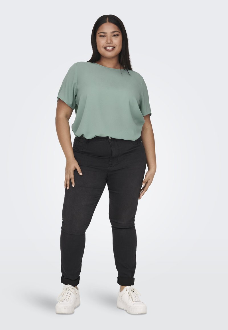 Blusa verde chiaro a maniche corte abbinata a jeans skinny neri, con due tasche anteriori, e sneakers bianche con suole testurizzate.