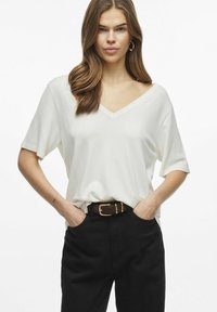 Top bianco leggero a V con maniche corte, abbinato a pantaloni neri a vita alta e una cintura marrone con una fibbia dorata.