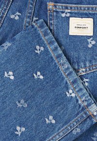 Tessuto in denim blu con motivo floreale bianco su piccola scala. Bordo cucito con un'etichetta che legge "BONPOINT" e dettagli di cuciture in contrasto.