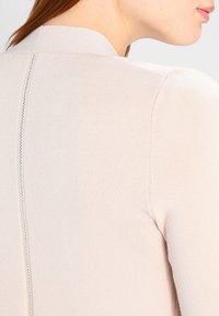 Gros plan sur le dos d'une femme portant un haut en tricot côtelé de couleur beige clair avec une couture verticale au centre.