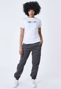 Camiseta de algodón blanca con texto gráfico en negro, combinada con pantalones cargo gris oscuro que tienen bolsillos y puños elásticos, y zapatillas blancas.