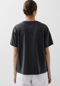 Dunkelgraues Baumwoll-T-Shirt mit kurzen Ärmeln, lockerer Passform und rundem Ausschnitt. Der Rücken hat einen geraden Saum und minimalistische Details.