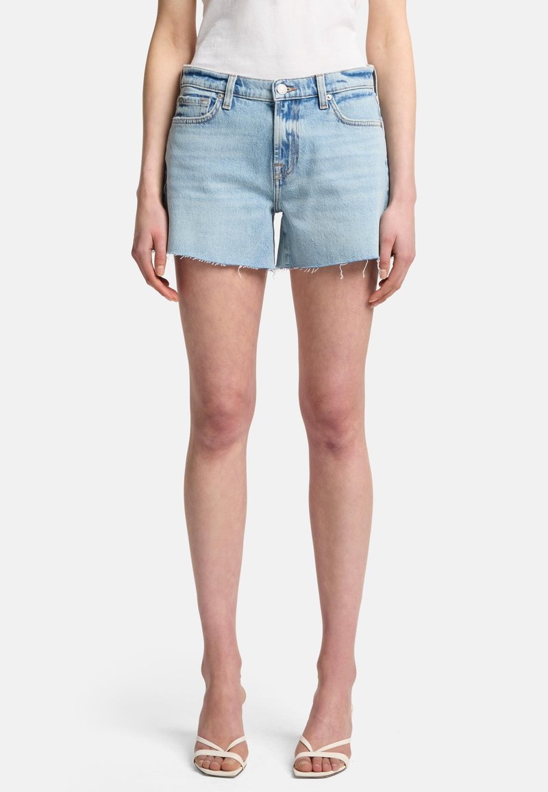 Ljusblå denimshorts med rå fåll, fem fickor och knäppning. Matchat med vita sandaler med remmar och en figurnära vit topp.