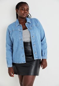 Gai zila džinsa jaka ar klasisku apkakli, pogu aizdari un garajām piedurknēm, kombinētā ar pelēku augšu un melnu ādas mini svārku.