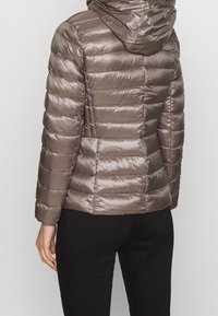 Vadderad, huva-jacka i metallisk taupe med en glänsande finish. Har horisontellt randig quiltad design och elastiska manschetter.