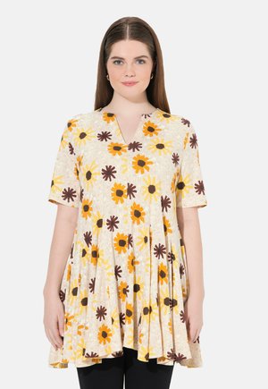 Tunique florale en crème avec des fleurs jaunes et brunes, à manches courtes, en col en V, et un design plissé. Fabriquée en tissu léger.