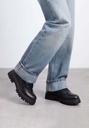 Scarpe stringate in pelle nera con suola in gomma spessa, caratterizzate da una finitura liscia e cuciture resistenti. Indossate con jeans in denim azzurro chiaro.