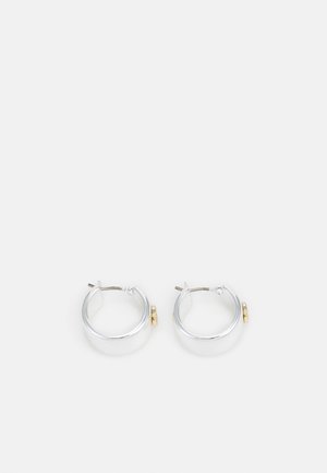 Boucles d’oreilles créoles en argent avec de petits charms ressemblant à des pièces d’or, présentées sur un fond blanc.