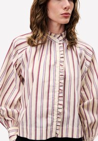 Lichte katoen blouse met verticale strepen in beige, rood en blauw. Rimpeldetail langs de knoopsluiting en volumineuze mouwen.