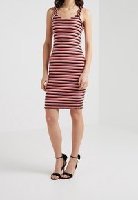 Gestreiftes Bodycon-Kleid mit dünnen Trägern, Rüschendetails, geripptem Material und den Farben Rot, Weiß und Marineblau. Kombiniert mit schwarzen, gestrickten Absatzschuhen.
