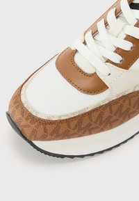 Sneaker med en kombinasjon av hvitt stoff og brunt lær med et mønstret beige akcent. Rundet tå, flate snører og svart såle.