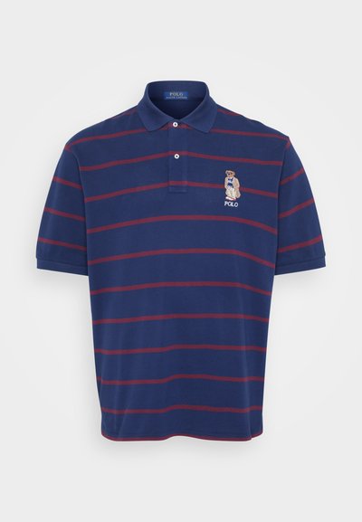 Polo de cor azul-marinho com riscas horizontais em marrom, colarinho de dois botões e logótipo de urso bordado no lado esquerdo do peito. Material de algodão, mangas curtas.
