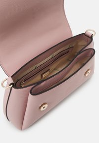 Jasnoróżowa torebka syntetyczna o teksturowym materiale, złotym okuciu i dwóch wewnętrznych przegrodach. Wewnątrz znajduje się beżowa podszewka z logo.