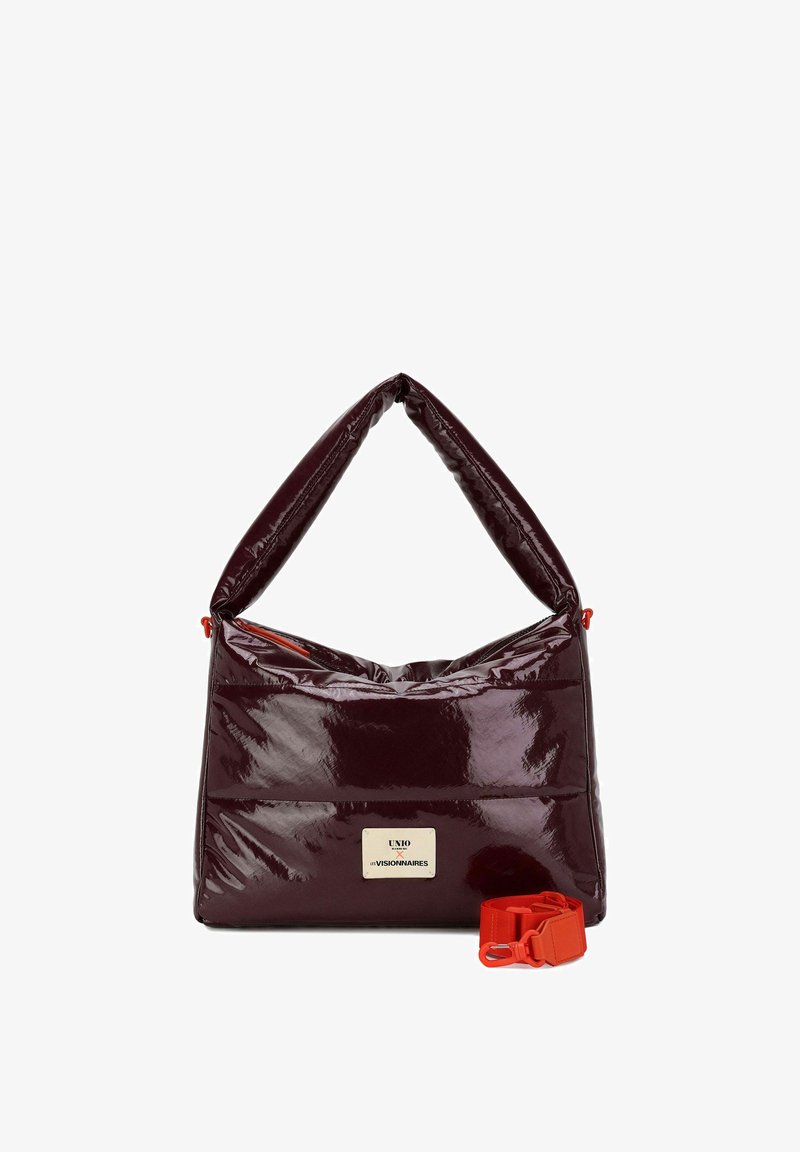 Bolso de mano de cuero charol burdeos con acabado brillante, diseño acolchado y una correa roja ajustable. Cuenta con una placa con el logo en el frente.