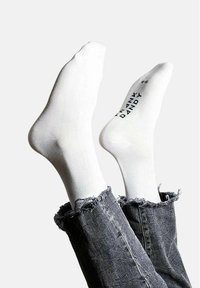 Vita bomullssockor med ribbad textur, med tryckt texten "FRANK DANDY" på sidan. Bärs ovanför nötta grå jeans.