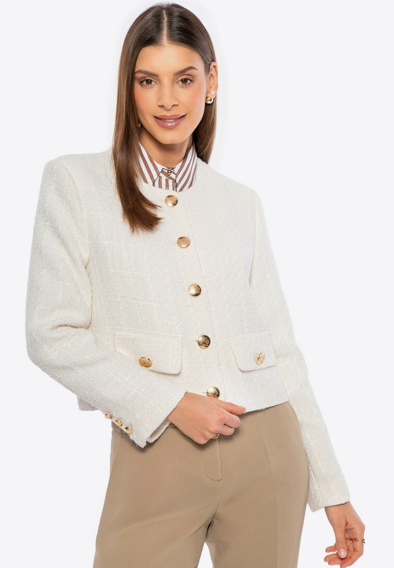 Giacca in tweed bianco con un design strutturato, bottoni dorati e due tasche frontali. Finiture con un collo arrotondato e tessuto testurizzato.