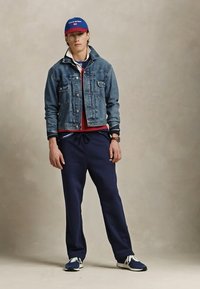 Traper jakna preko crvene majice, mornarskih tregersica i plavih tenisica. Plava kapa s crvenim detaljima upotpunjuje odjevnu kombinaciju. Ležeran i sportski stil.