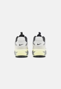 Nike-sneakers med en grå, svart och vit ovandel, en texturerad gul sula och dragflikar vid hälarna för enkel påtagning.