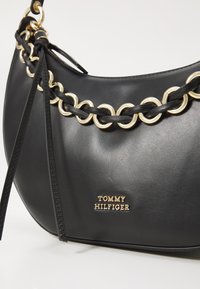 Borsa a spalla in pelle nera con accentuazione in catena dorata, dettagli intrecciati e placca con logo dorato. Texture liscia con forma strutturata.
