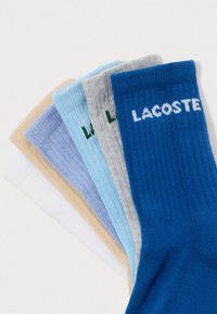 Penki poros sulankstytų kojinių baltos, smėlio, šviesiai purpurinės, šviesiai mėlynos, pilkos ir mėlynos spalvos su "LACOSTE" tekstu ant apykaklės.